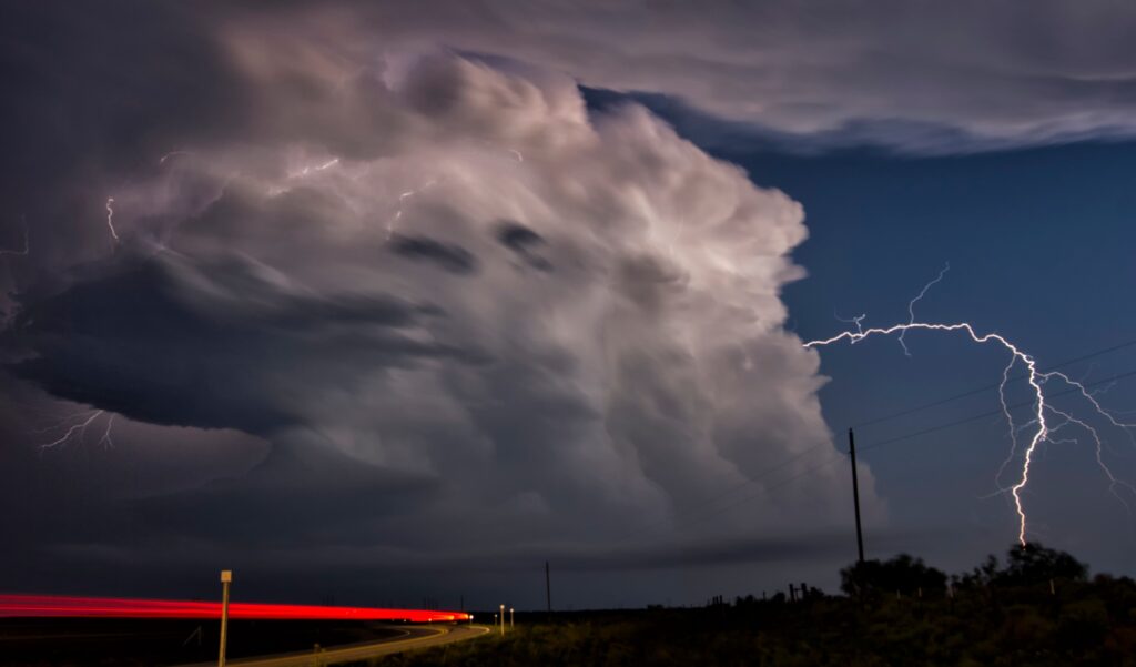 Vehicle light trails and lightning bolt arcing laterally from storm cloud